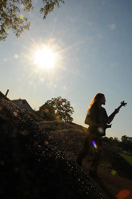 Silhouette of a guitarist playing on a hillside against a bright sunburst