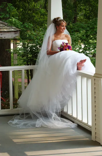 Bride sitting on a porch railing with her veil spilling to the floor