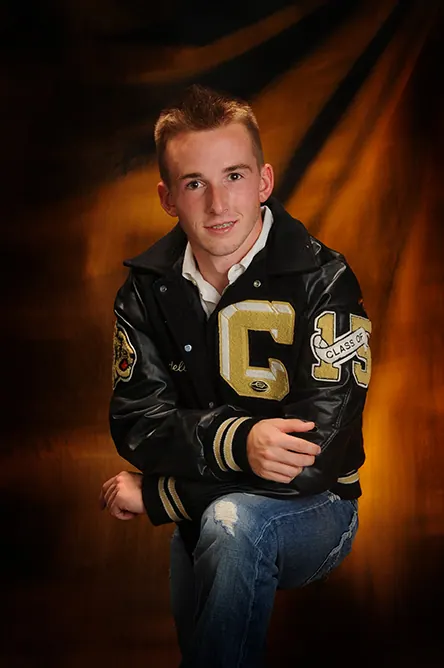 Studio portrait of a senior in a black and gold letterman jacket