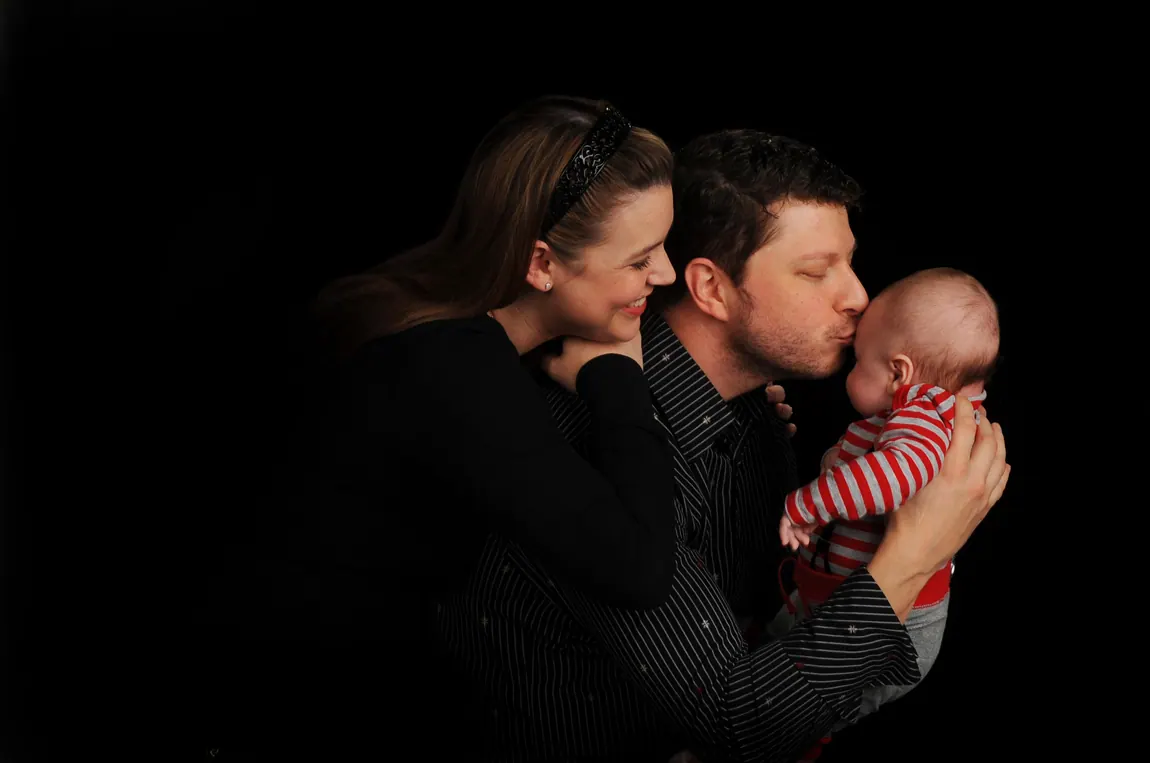 Parents kissing their baby in a low-key studio portrait