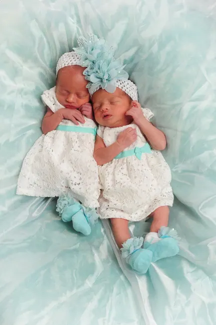 Newborn twin girls in white dresses and headbands on mint fabric
